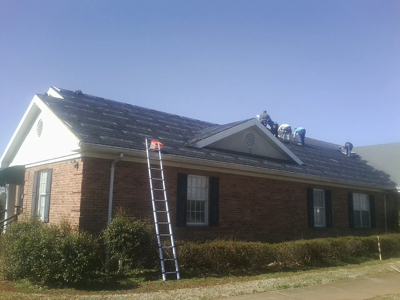 Crew tearing shingles off a brick ranch roof with a ladder set — Emergency Roof Repair work by our crew in Starrucca