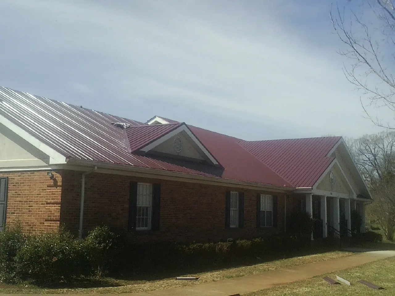 Red metal roof with gabled entries on a long brick building, from a Hail Damage Roof Repair job in Starrucca