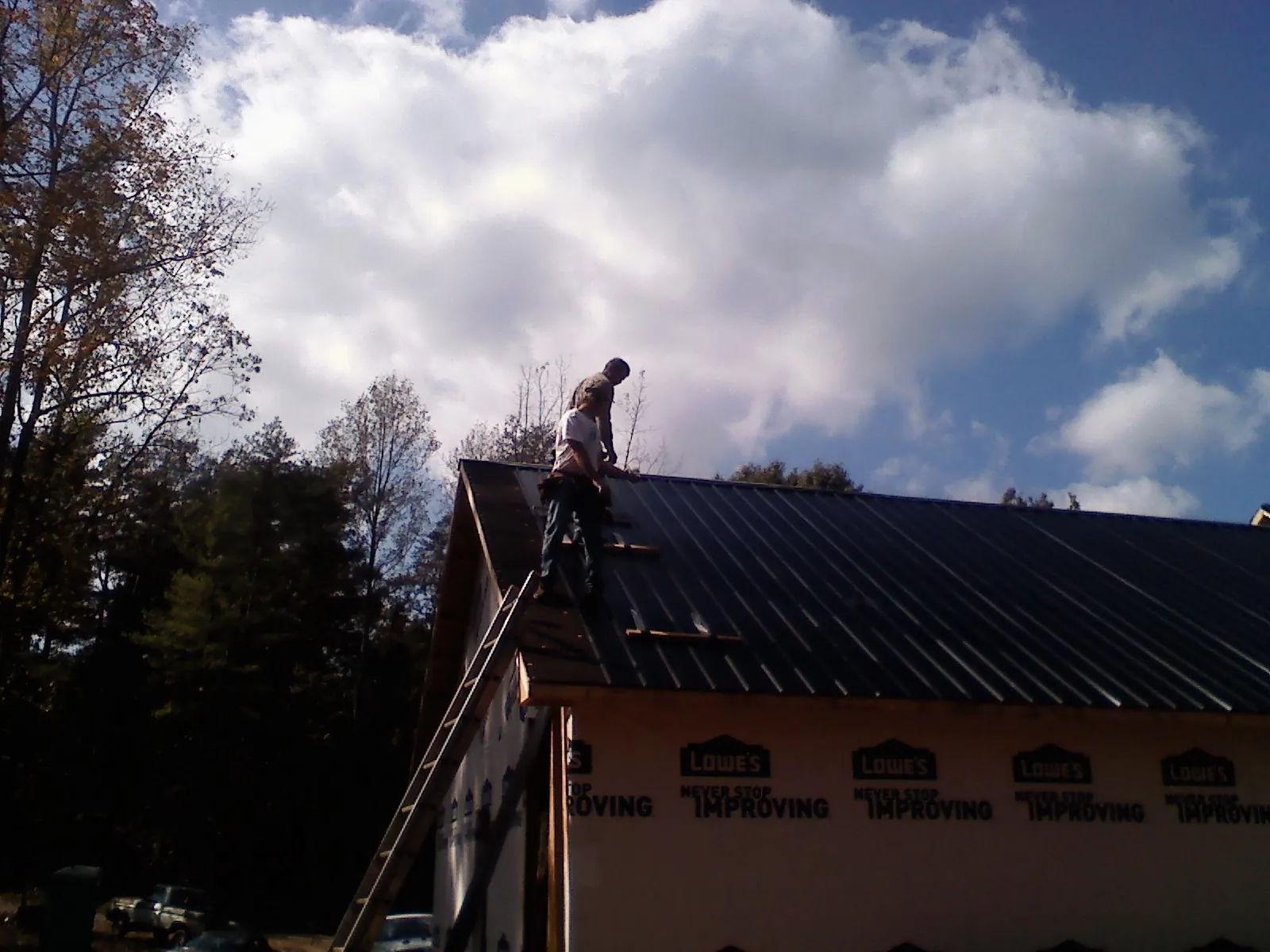 Roofer fastening dark metal panels high against a cloudy sky, from a Roof Inspection job in Starrucca