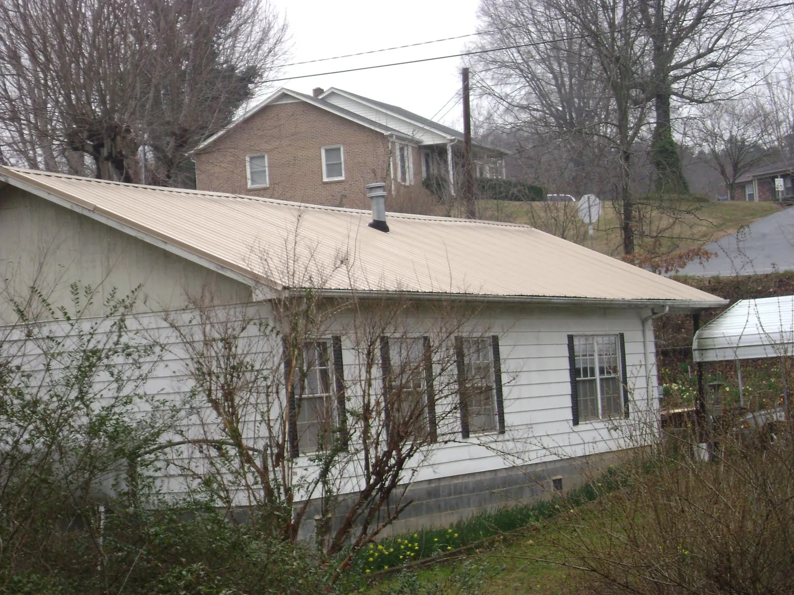 Tan metal roof on a white sided house set into a hillside — Commercial Roofing by Roofing Brothers in Starrucca