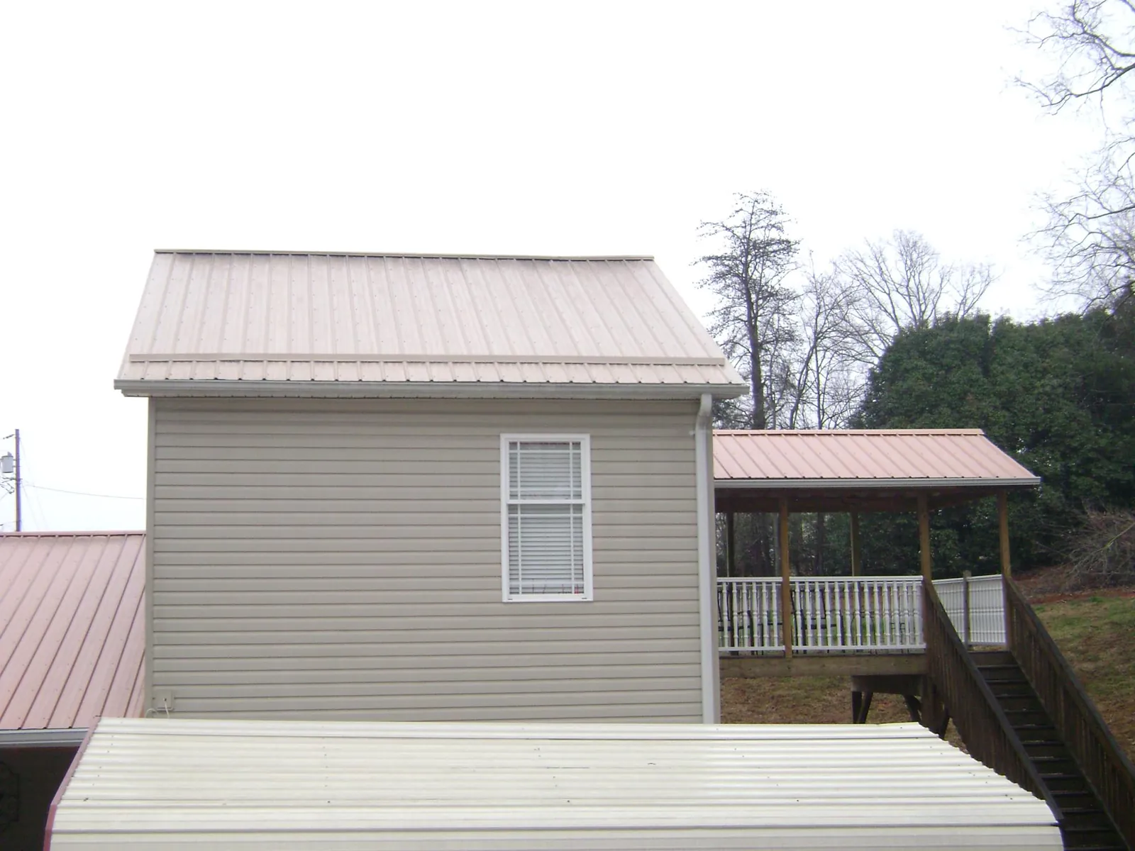 Tan metal roofs on a two story addition and attached porch, from a Roof Replacement job in Starrucca